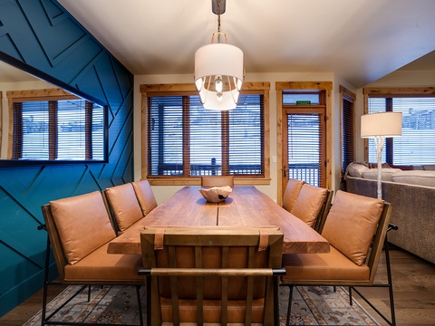 Gather around your stunning handcrafted dining table beneath modern pendant lighting. The bold teal accent wall and wraparound windows create a bright, inviting space for memorable meals together.