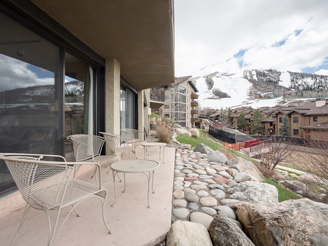 Balcony overlooking a mountain resort village, featuring ski slopes, neighboring buildings, and natural rock formations in the surrounding area.