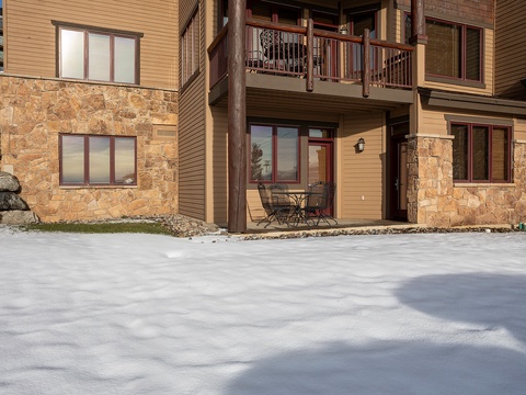 Mountain-style vacation condo featuring warm stone and wood exterior with private patio entrance and balcony access in a peaceful alpine setting.