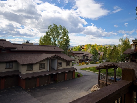 Property exterior captures a peaceful residential setting with mountain views and mature trees framing the neighborhood, photographed during daytime with dramatic clouds overhead.