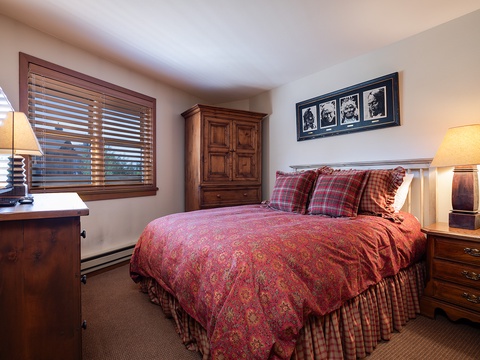 Settle into your cozy bedroom with warm wood furnishings, a plush queen bed dressed in inviting linens, and soft lamplight that creates the perfect retreat after a day of adventure.