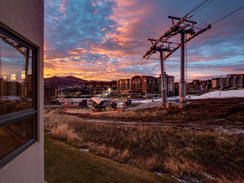 The property overlooks a mountain resort village with ski gondola infrastructure and dramatic sunset views over the surrounding peaks and buildings.