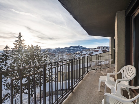 Mountain retreat balcony with sweeping views of snow-covered peaks and trees, featuring outdoor seating perfect for sipping morning coffee in the crisp alpine air.