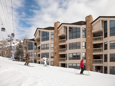 Multi-story vacation property with stone chimneys and balconies sits slope-side, offering direct ski-in/ski-out access at a mountain resort with lift visible overhead.