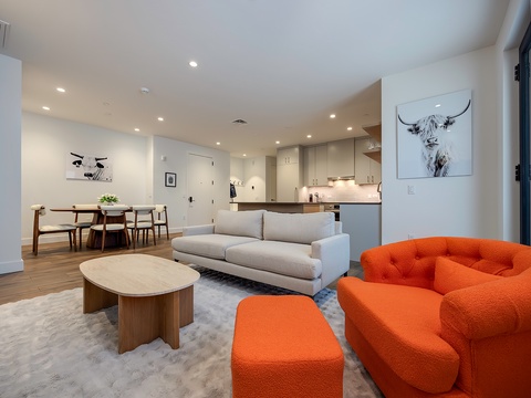 Picture yourself settling into this bright, open space where contemporary design meets comfort. The bold orange seating catches your eye while warm wood tones invite you to unwind after exploring.