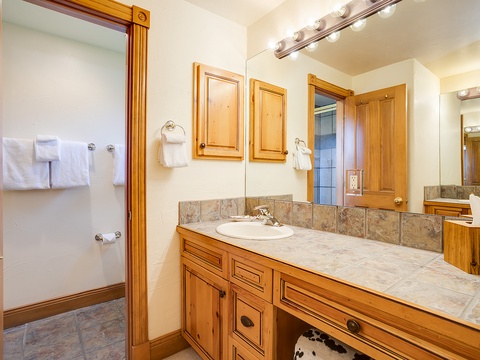 Your private bathroom features warm wood cabinetry, tile countertops, plush towels, and bright vanity lighting to help you feel right at home.