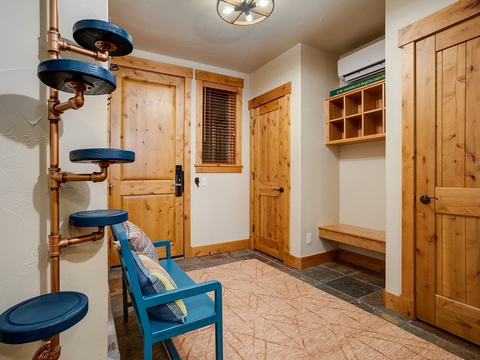 A charming entryway greets you with warm wood tones and a whimsical copper cat tower. Store your belongings in the bench and wardrobe before relaxing in the cozy blue chair.