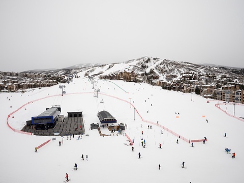 A scenic ski resort with well-groomed slopes, chair lifts, and lodge facilities nestled at the base of snow-covered mountains, surrounded by resort accommodations.
