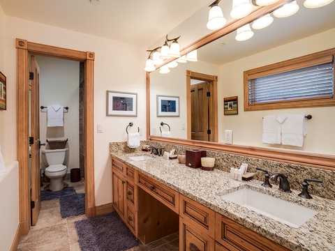 Step into your private sanctuary with a spacious dual-vanity bathroom featuring warm wood cabinetry, granite countertops, and fresh towels awaiting your arrival—thoughtfully designed for your comfort.