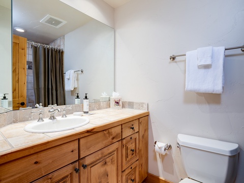 Your private bathroom features warm wood cabinetry, a spacious vanity with fresh towels, and a walk-in shower behind the curtain—clean, comfortable, and ready for you.