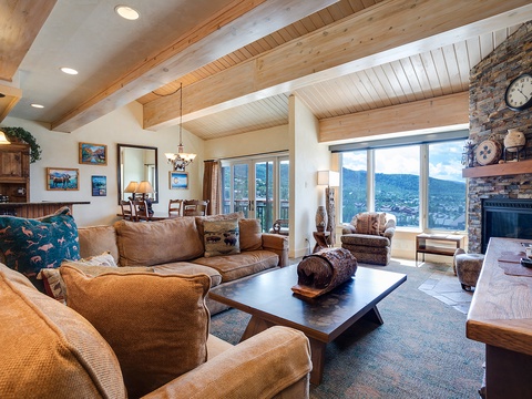 Settle into plush seating surrounded by warm wood beams and a stone fireplace while soaking in stunning mountain views through floor-to-ceiling windows. Your perfect mountain retreat awaits.