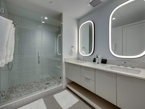 Your modern bathroom features a spacious walk-in shower with elegant tilework, double vanity with backlit mirrors, and plush white towels ready for you.