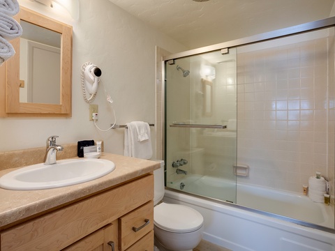 Your well-appointed bathroom features a spacious tub-shower combo, warm wood cabinetry, and thoughtful touches like fresh towels and a hairdryer for your convenience.