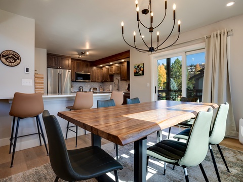 Gather around your large wooden dining table for meals together while the chandelier glows overhead. The open kitchen with stainless appliances invites shared cooking moments and the view outdoors extends your space beautifully.
