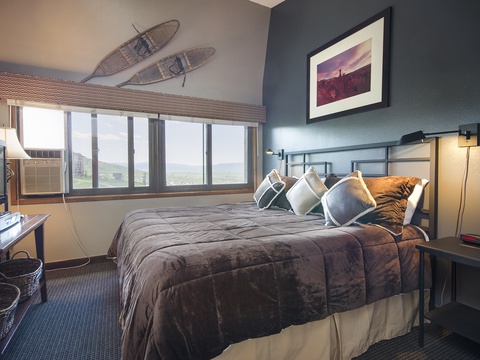 Drift off in your cozy bedroom featuring mountain-inspired décor, plush bedding, and sweeping views of rolling hills through large windows that fill your space with natural light.