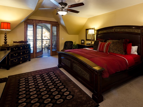 Step into your spacious bedroom retreat, where rich wood furnishings and a luxurious king bed draped in deep red await. Vaulted ceilings and a private balcony complete your peaceful haven.