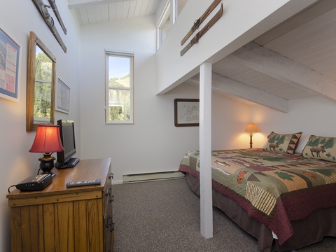 Your peaceful retreat features a cozy bedroom with a lofted sleeping area, rustic wood accents, and abundant natural light streaming through tall windows overlooking the surrounding landscape.