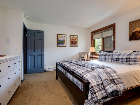 Unwind in your cozy bedroom with plaid bedding, wood accents, and mountain-inspired art. Enjoy natural light from the window and ample storage in the dresser for your belongings.