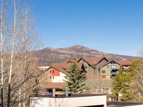 The property is located in a scenic mountain setting with dramatic peaks rising behind colorful multi-story buildings surrounded by aspen and evergreen trees.