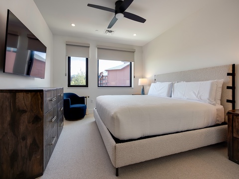 Sink into crisp white linens and watch natural light spill through oversized windows. Your modern bedroom retreat features custom wood furnishings, a cozy reading chair, and a whisper-quiet ceiling fan to keep you comfortable.