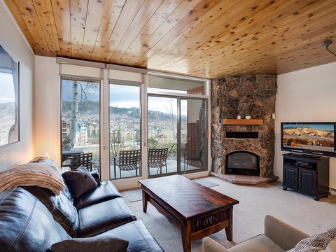 Relax in this inviting living space with a striking stone fireplace, warm wood-planked ceiling, and mountain views through your private balcony doors.