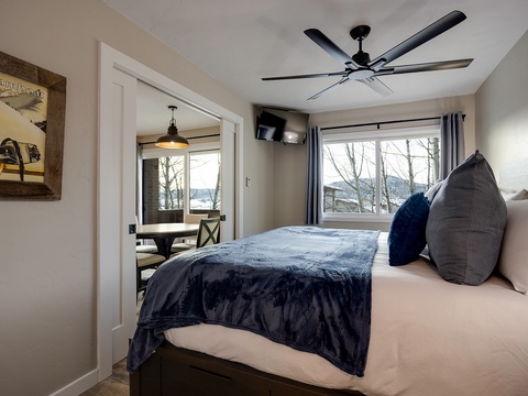Unwind in your peaceful bedroom, where plush bedding, a ceiling fan, and serene lake views through large windows create the perfect retreat after a day of adventure.