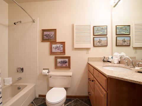 Your private bathroom features a tiled tub-shower combo, wood vanity with granite counters, and charming Western artwork that captures the spirit of the surrounding area.