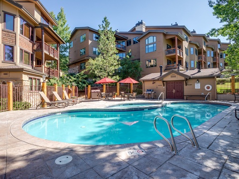 Sun-soaked pool awaits, surrounded by towering pines and mountain-style architecture. Lounge chairs and shaded seating invite relaxation after your alpine adventures, making this your perfect retreat to unwind.