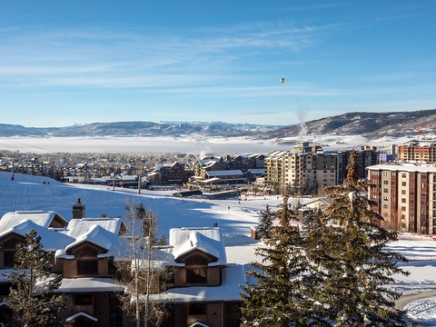 A picturesque winter resort village with snow-draped chalets, ski slopes, and mountain lodges under clear blue skies—ideal for a serene alpine getaway.