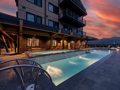 A stunning evening awaits at this modern rooftop pool area, where warm waters glow beneath a painted mountain sunset sky. Contemporary covered seating areas frame the space, perfect for relaxation after a day of adventure.