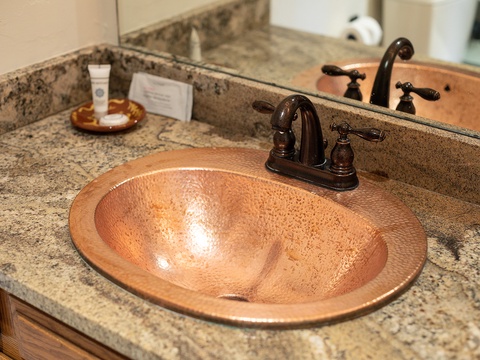 Elegant hammered copper sink with rich bronze fixtures and granite counters adds warmth to your private bathroom retreat.