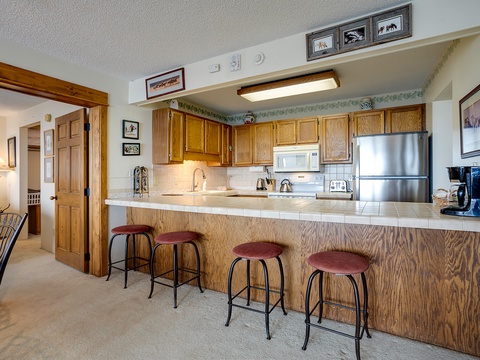 Your fully equipped kitchen features oak cabinetry, stainless steel appliances, and a welcoming breakfast bar with seating, perfect for preparing meals and gathering together.