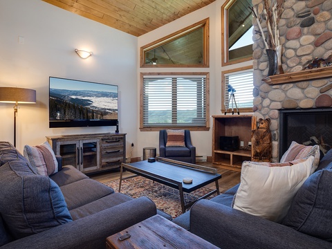 Sink into plush couches, warm your toes by the stone fireplace, and watch mountain vistas on the big screen—your cozy alpine retreat awaits with vaulted wood ceilings and rustic charm.