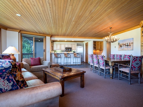 Relax in this spacious open-plan living area where rustic wood ceilings meet vibrant patterned accents. Your dining table awaits family meals, while plush seating invites cozy evenings.