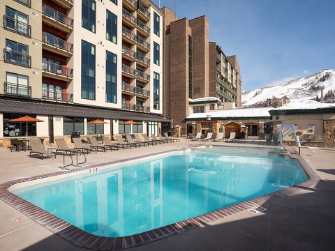 Sparkling heated pool surrounded by comfortable loungers, with dramatic mountain views providing a stunning alpine backdrop just steps from your vacation rental.