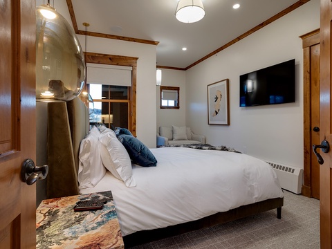 Relax in your cozy bedroom featuring a plush bed, warm wood accents, and a wall-mounted TV—your peaceful mountain retreat awaits after a day of adventure.