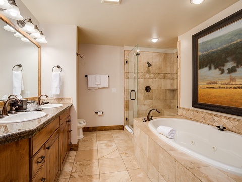 Unwind in your spacious bathroom featuring a deep soaking tub with jets, walk-in shower, dual vanities, and warm mountain-inspired décor.