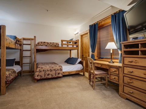 Two bunk beds and a twin sleep up to five comfortably in this cozy room, featuring warm wood furnishings, a dedicated workspace, and a mounted TV for downtime entertainment.