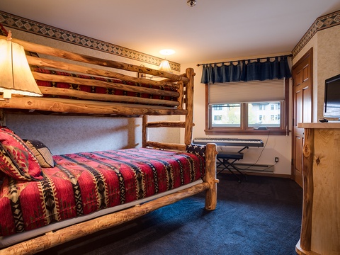 Your rustic retreat awaits with handcrafted log bunk beds dressed in vibrant Southwestern-style bedding, where cozy wood details and warm lighting create the perfect mountain escape for families.