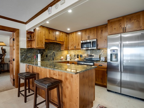 Your fully-equipped kitchen features rich wood cabinetry, gleaming granite counters, stainless steel appliances, and a breakfast bar perfect for morning coffee or casual meals.