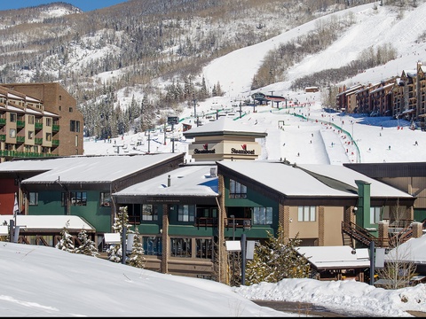 A winter ski village surrounded by snow-covered mountains, ski slopes, and lodges in a scenic alpine setting.