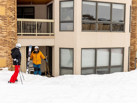 Two skiers arriving at this winter retreat with equipment in hand, ready to hit the slopes right from their doorstep, surrounded by fresh mountain snow.