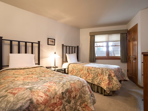 You'll love waking up in this cozy twin bedroom, with its two plush beds dressed in floral comforters, warm lighting, and peaceful mountain views peeking through the window.