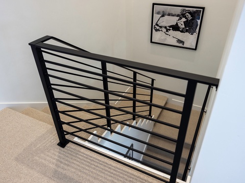 A sleek black metal staircase railing adds modern style, accented by a charming vintage photograph on the wall.