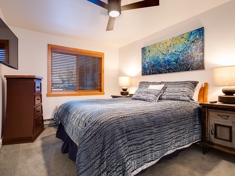 Sink into soft linens and drift off beneath a vibrant coastal artwork. Warm bedside lamps and a peaceful ceiling fan create your perfect retreat after a day of mountain adventures.