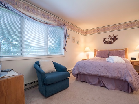 Unwind in your cozy retreat with a plush bed, comfy armchair for reading, and soft natural light from large windows. Your peaceful mountain getaway awaits.