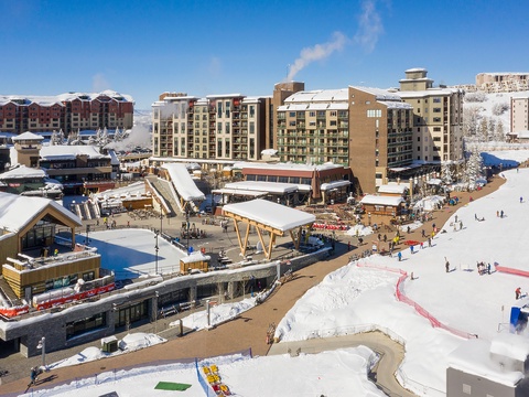 This aerial view captures the vibrant ski village base, showcasing snow-covered slopes, lodges, dining options, and entertainment facilities nestled in the heart of winter mountain scenery.