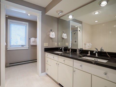 Your private bathroom offers dual sinks with gleaming black countertops, ample storage, and fresh white towels, all bathed in natural light from a sunny window.