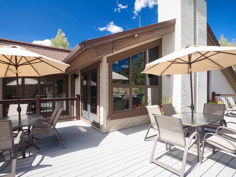 This spacious deck offers shaded seating under cream umbrellas, with mountain views and direct access to the home's bright, windowed living spaces—ideal for outdoor dining and relaxation.