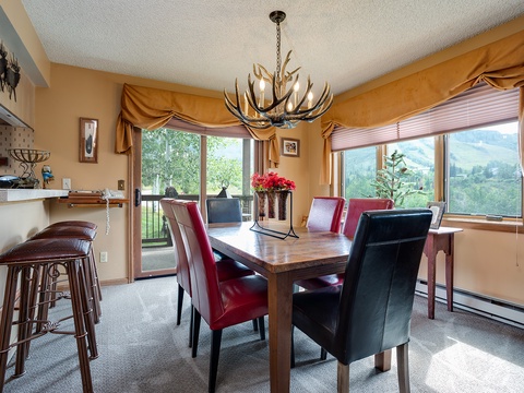 Gather around this handsome dining table beneath a striking antler chandelier, with mountain views framing your meals and sliding doors opening to the fresh air beyond.